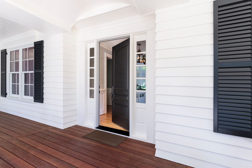 Front porch area with black door, white trim, siding, and wood plank flooring