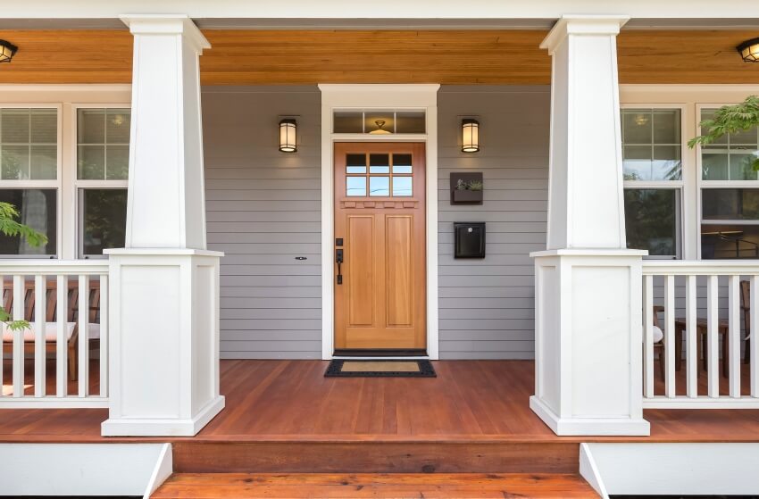 Front porch of a home with solid wood door, sconce lights, and nickel gap shiplap siding