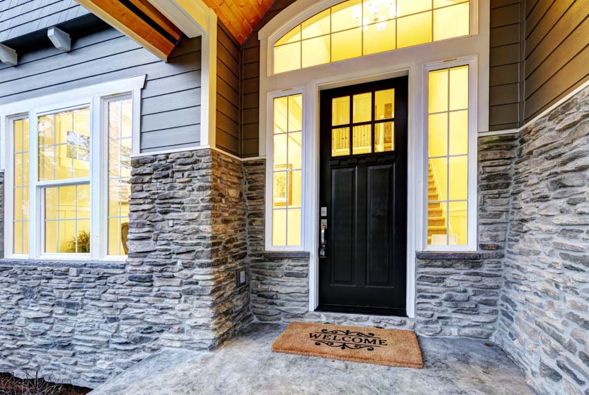 Front porch with black door, windows, white trim, and stone wall cladding
