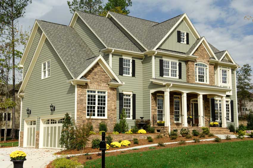 Green and brown house exterior with siding, windows, pitched roof, front porch, walkway, and hedge plants