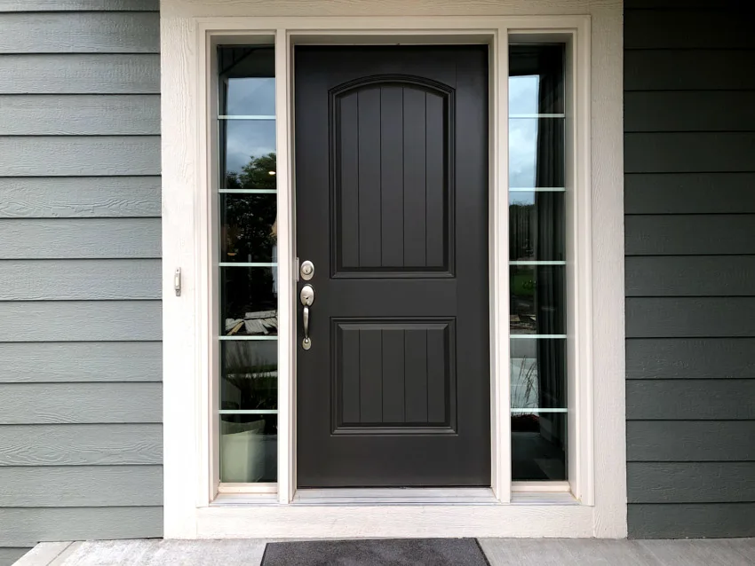 House with black paneled door, glass sidelight panels, white trim-work, and grey siding