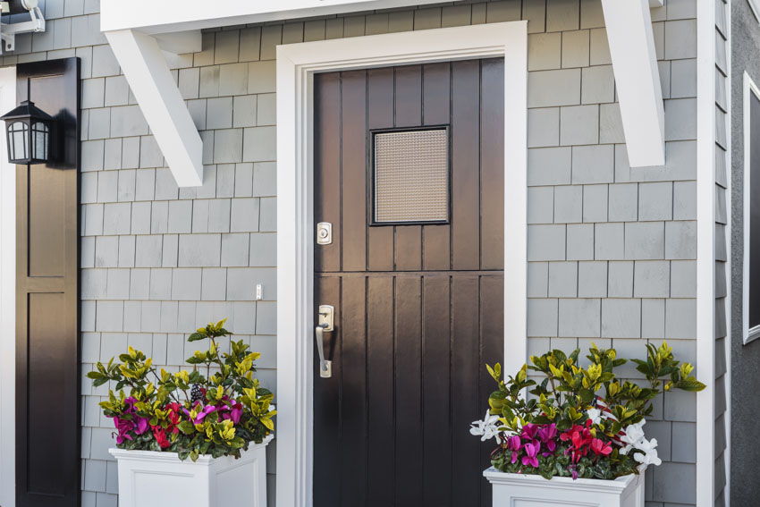 House exterior with black front door, white trim, shingle siding, and potted flowers