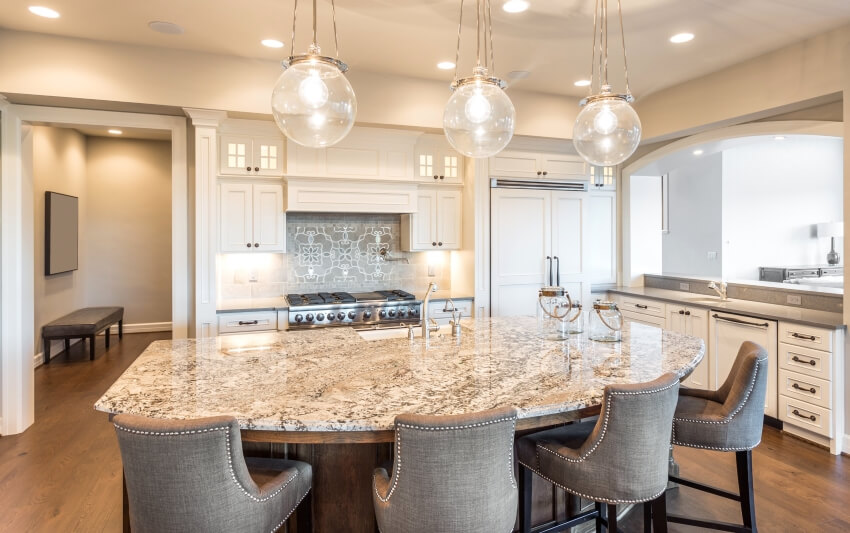 Island with brown granite countertops and chairs in a kitchen with stylish pendant lights