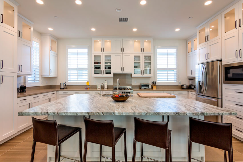 Kitchen with large island, leather stools, recessed lighting and cabinets with black pulls