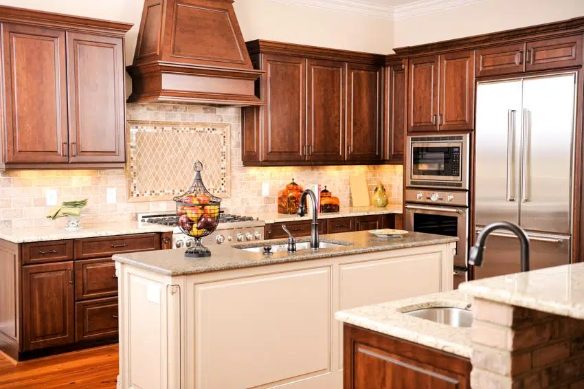 Kitchen with beige backsplash, island, countertops, cherry cabinets, sink, faucet, and range hood