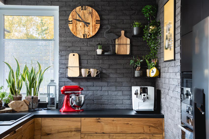 Kitchen with black brick backsplash, countertop, cabinets, indoor plants, and window