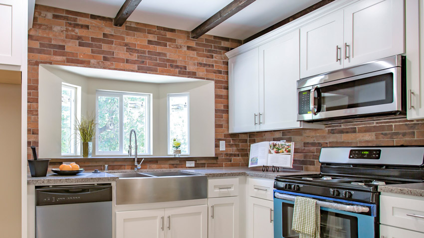 Kitchen with brick backsplash, white cabinets, sink, faucet, countertop, oven, and window