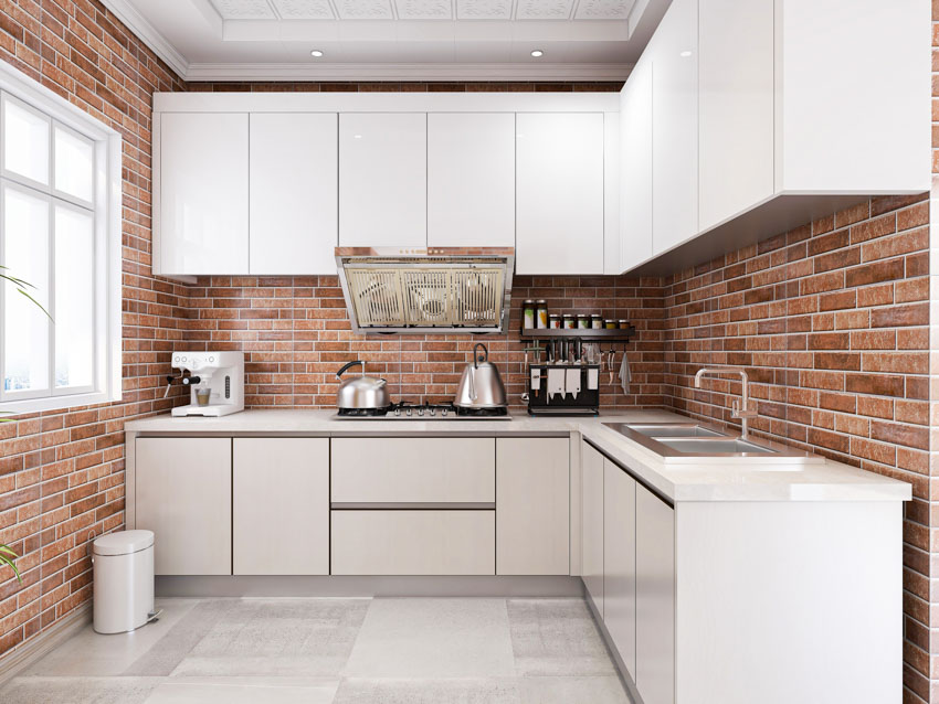 Kitchen with brick veneer backsplash, countertop, range hood, stove, cabinets, and window