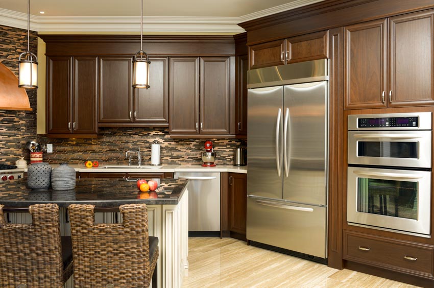 Kitchen with brown melamine cabinets, wood floors, pendant lights, tile backsplash, refrigerator, and oven