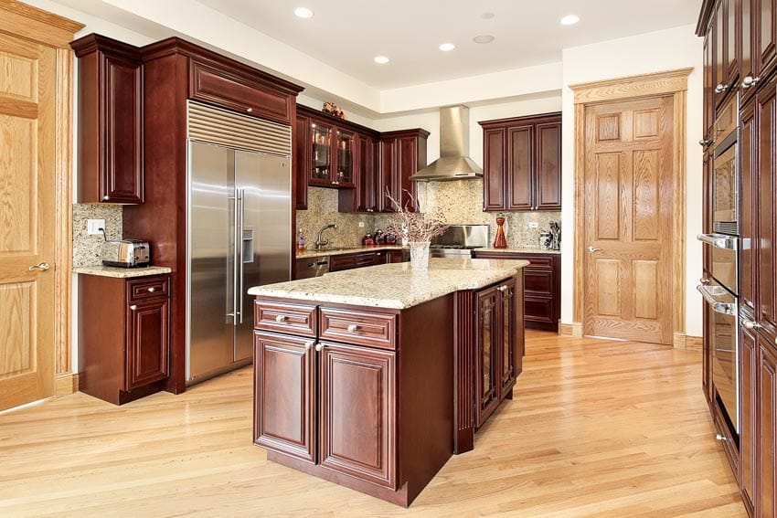 Kitchen with cherry cabinets, island, countertops, backsplash, refrigerator, range hood, and wood floors