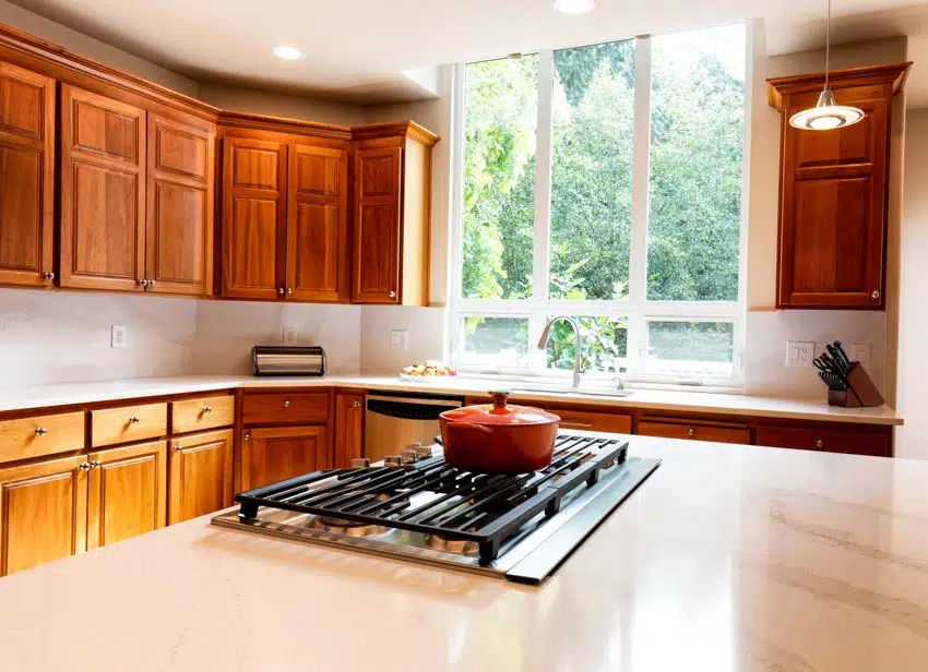 Kitchen with cherry cabinets, white backsplash, countertops, stove, and window