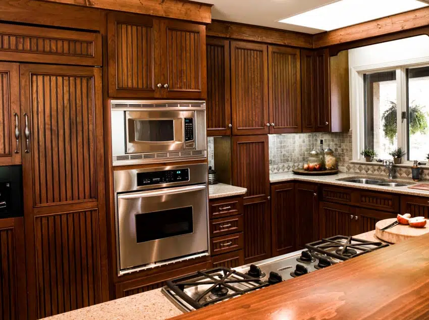 Kitchen with cherry wood cabinets, oven, stove, gray, backsplash, and windows