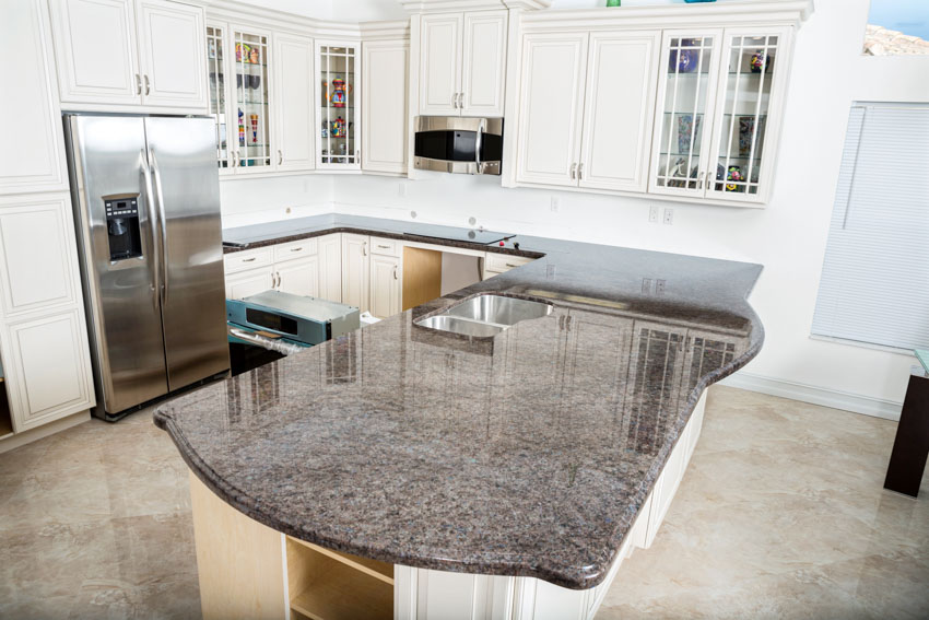 Kitchen with dark gray granite countertop, white cabinets, backsplash, and refrigerator