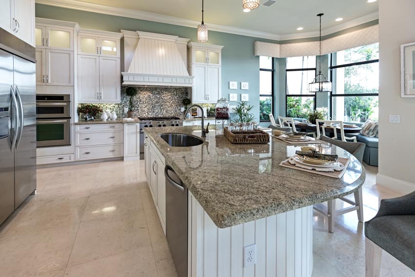 Kitchen with fantasy gray granite countertop, island tile floors, cabinets, windows, range hood, stove, and refrigerator