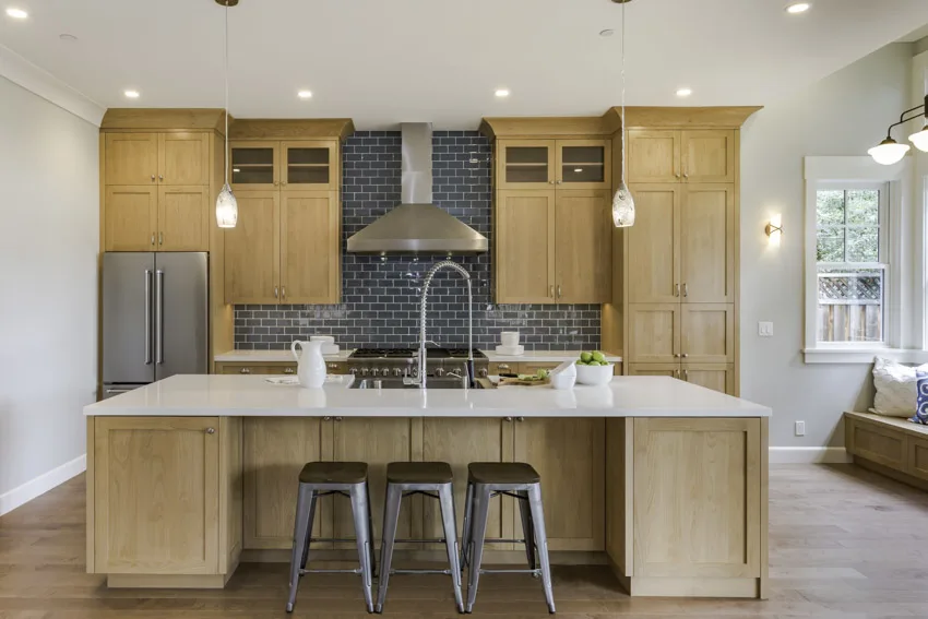 Kitchen with island, backsplash, poplar cabinets, range hood, countertops, stools, pendant lights, and wood flooring