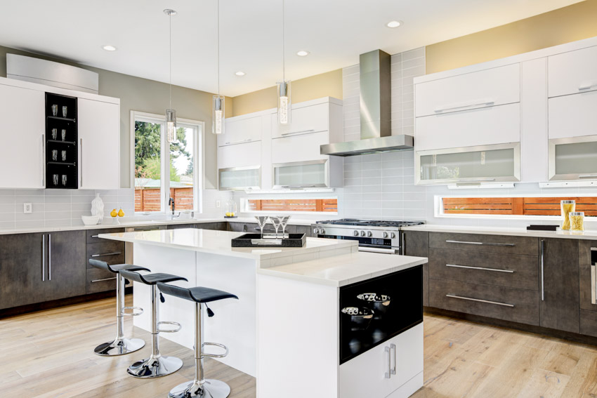 Kitchen with island, bar stools, frosted glass cabinets, range hood, backsplash, ceiling lights, and window