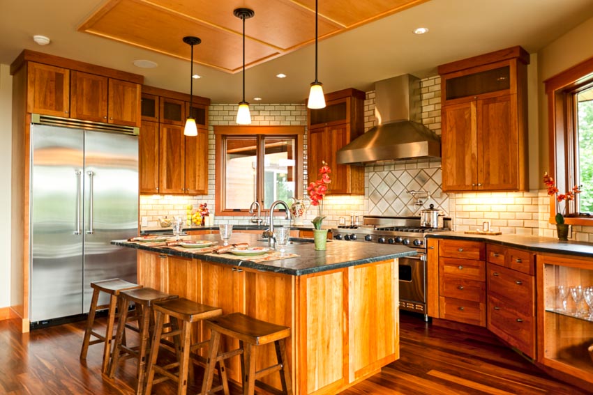 Kitchen with island, countertops, bar stools, natural wood cabinets, pendant lighting, tile backsplash, refrigerator, and windows