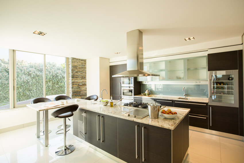 Kitchen with island, range hood, bar stools, countertops, backsplash, windows, and frosted glass cabinets