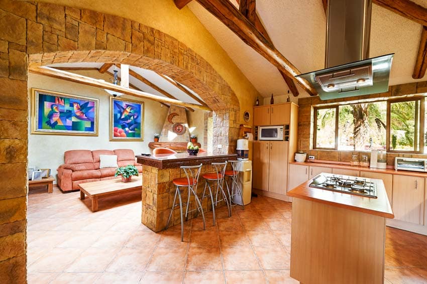 Kitchen with island, stove, bar, stools, counter, range hood, terracotta tile floor, and window