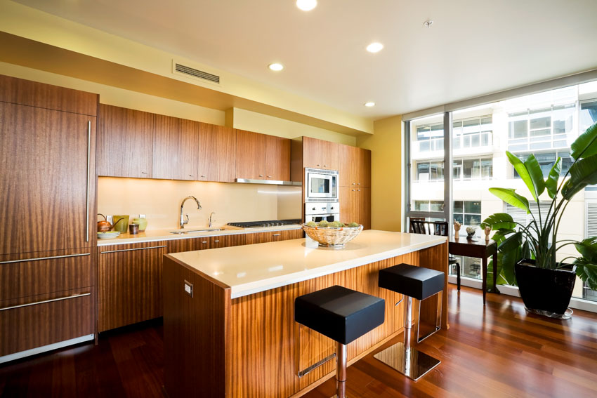 Kitchen with black bar stolls, large potted plant, wood island with white countertop