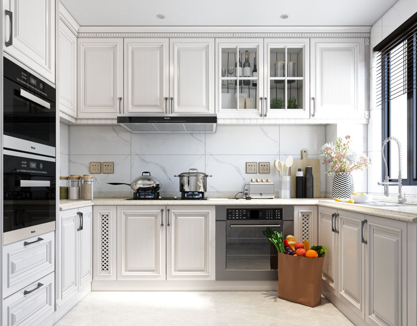 Kitchen with large backsplash tiles, stove with pots and under counter cabinets