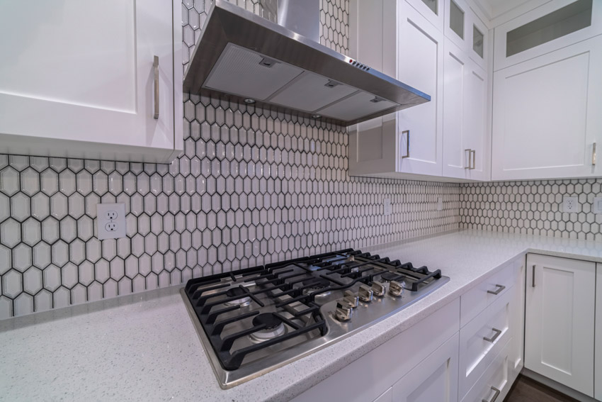 Kitchen with metal picket tile backsplash, stove, range hood, and white cabinets