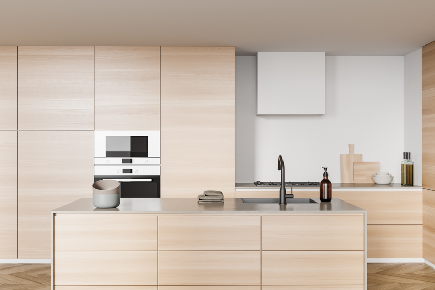 Kitchen with modern beech cabinets, island, countertop, range hood, faucet, sink, and oven
