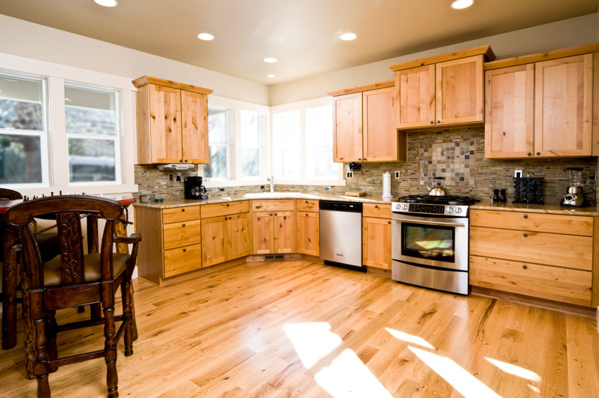 Kitchen with natural alder wood cabinets, wooden floors, backsplash, ceiling lights, oven, chairs, and windows