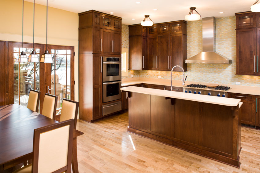 Kitchen with natural maple wood cabinets, island, countertops, backsplash, range hood, wood flooring, and ceiling lights