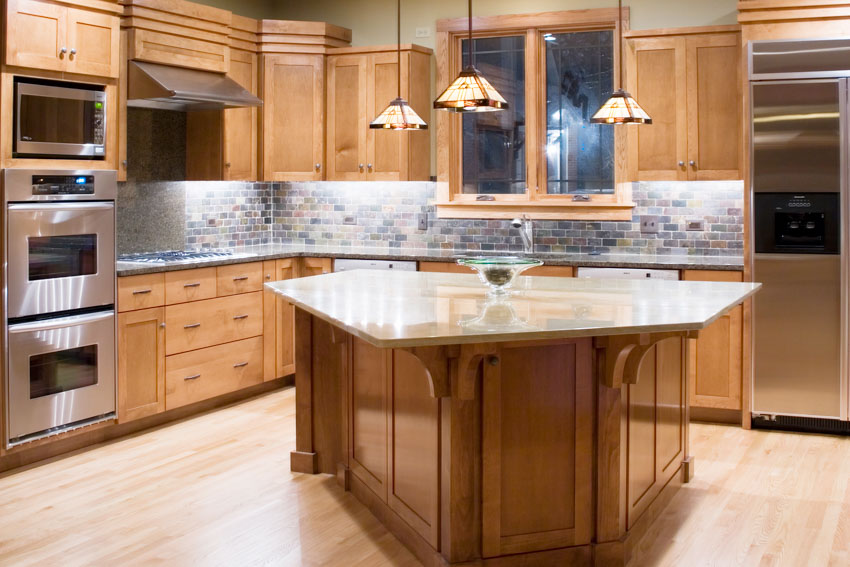 Kitchen with oak cabinets, brick tile backsplash, island, countertops, oven, and pendants