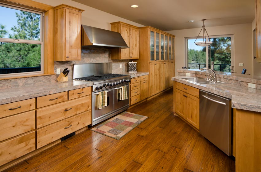 Kitchen with oak cabinets, handles, wood flooring, range hood, backsplash, countertops, and windows