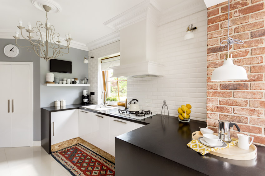Kitchen with painted brick backsplash, countertop, sink, range hood, shelves, window, and chandelier