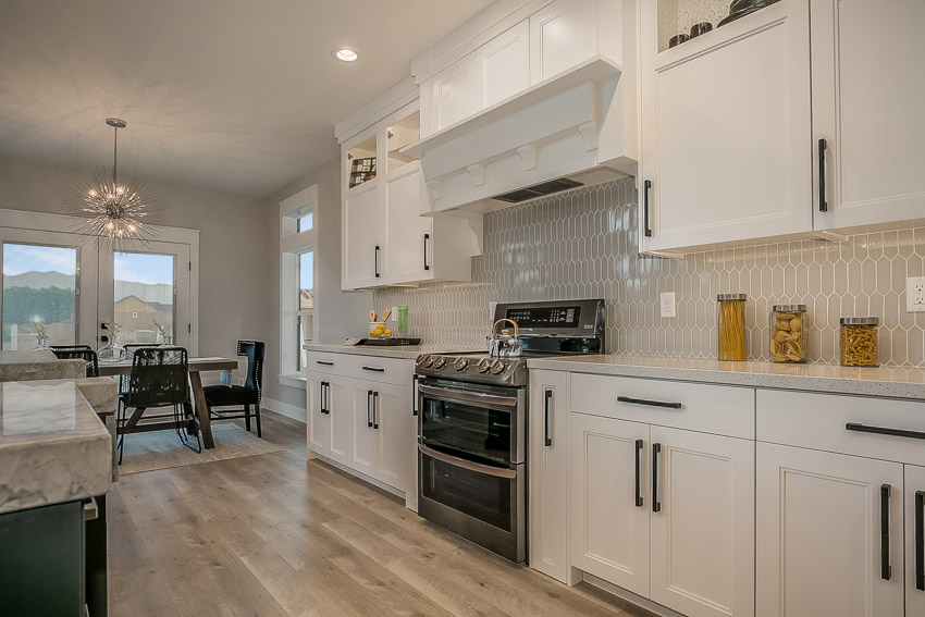 Kitchen with elongated hexagon tile backsplash, countertop, white cabinets, wood floors, range hood, stove, and oven
