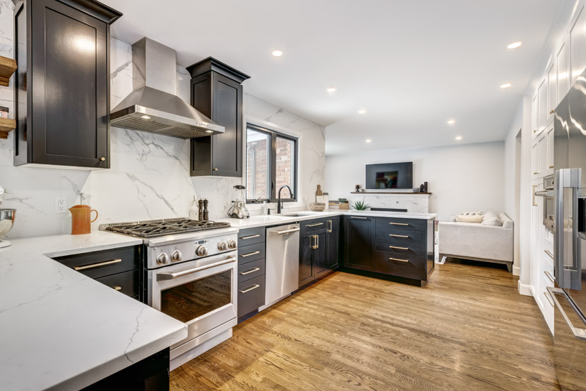 Kitchen with porcelain slab backsplash, countertop, wood flooring, cabinets, stove, range hood, oven, and ceiling lights