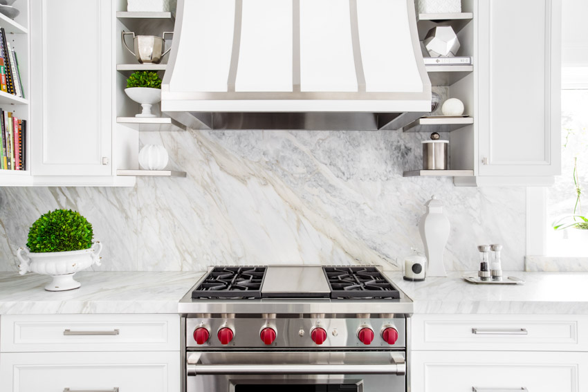 Kitchen with porcelain slab marble look backsplash, stove, range hood, and cabinets