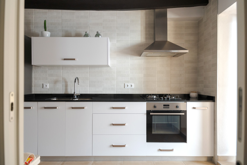 Kitchen with porcelain tile backsplash, cabinets, range hood, countertop, sink, and faucet