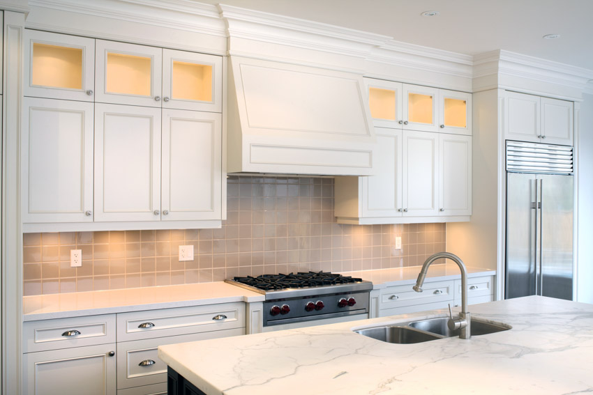 Kitchen with recessed cabinets, tile backsplash, range hood, stove, countertops, sink, and faucet