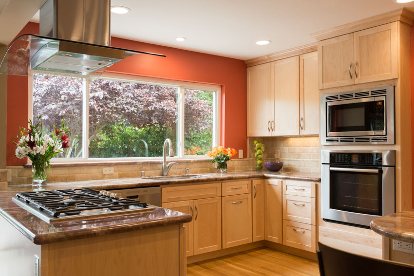 Kitchen with red wall, window, beech cabinets, oven, countertop, stove, and range hood