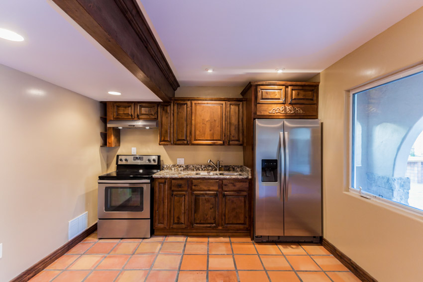 Kitchen with Saltillo tile floors, oven, backsplash, cabinets, refrigerator, and window