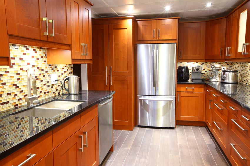 Kitchen with shaker recessed cabinets, mosaic tile backsplash, refrigerator, countertops, sink, and cabinets