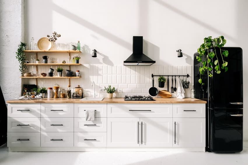 Kitchen with shelves, range hood, wood countertop, range hood, cabinets, vertical tile, backsplash, refrigerator, and indoor plant