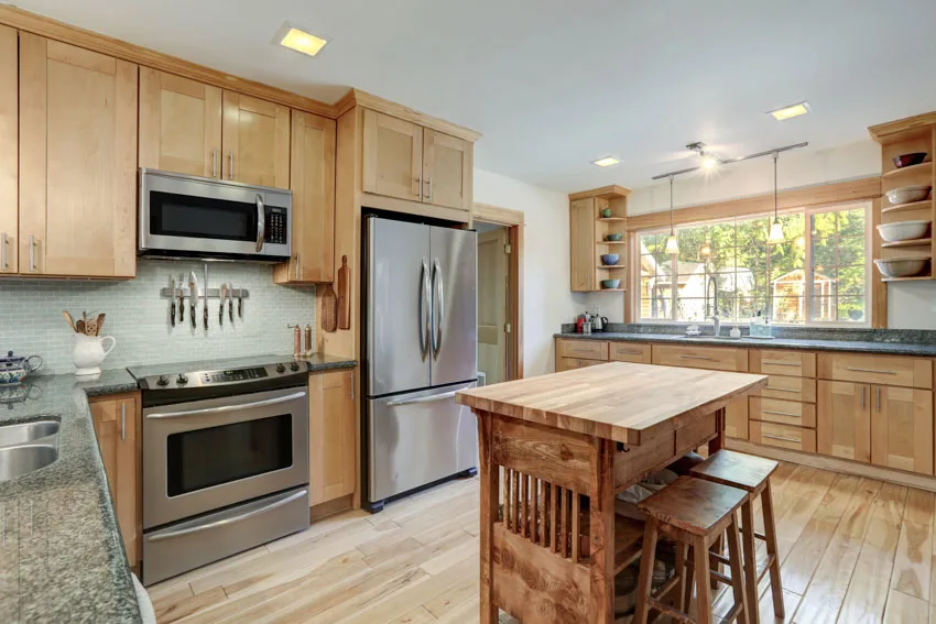 Kitchen with small island, countertop, stools, poplar cabinets, oven, refrigerator, and windows