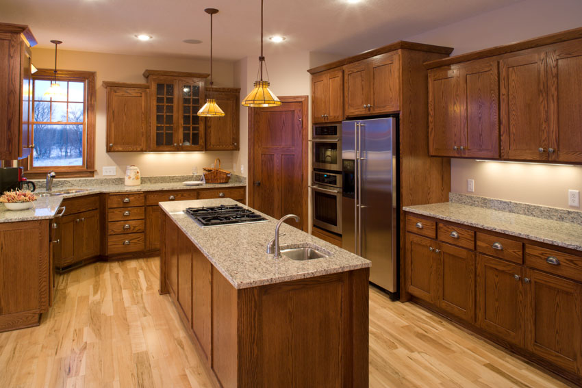 Kitchen with solid wood cabinets, island, countertop, wooden floors, backsplash, pendant lights, and refrigerator