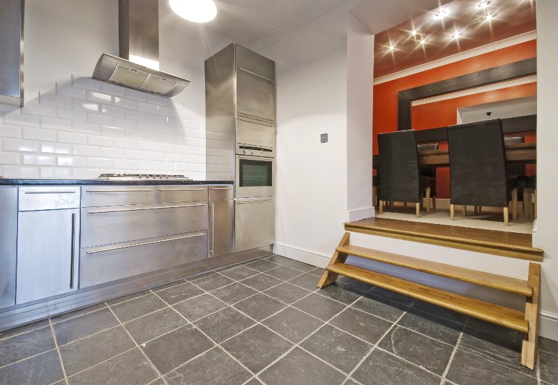 A kitchen features SPC flooring with stainless steel counter and appliances and two steps stairs going to dining area