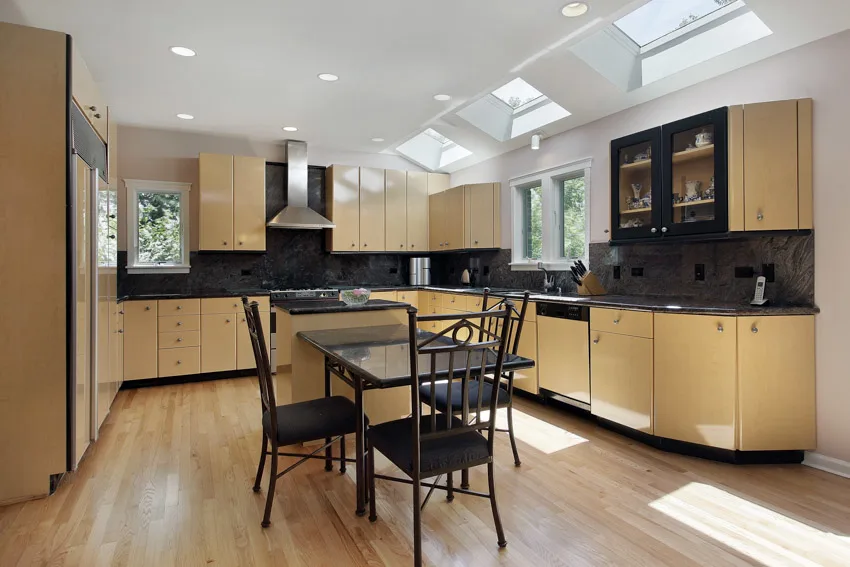 Kitchen with stained poplar cabinets, wood floors, table, chairs, countertop, backsplash, skylight windows, and range hood