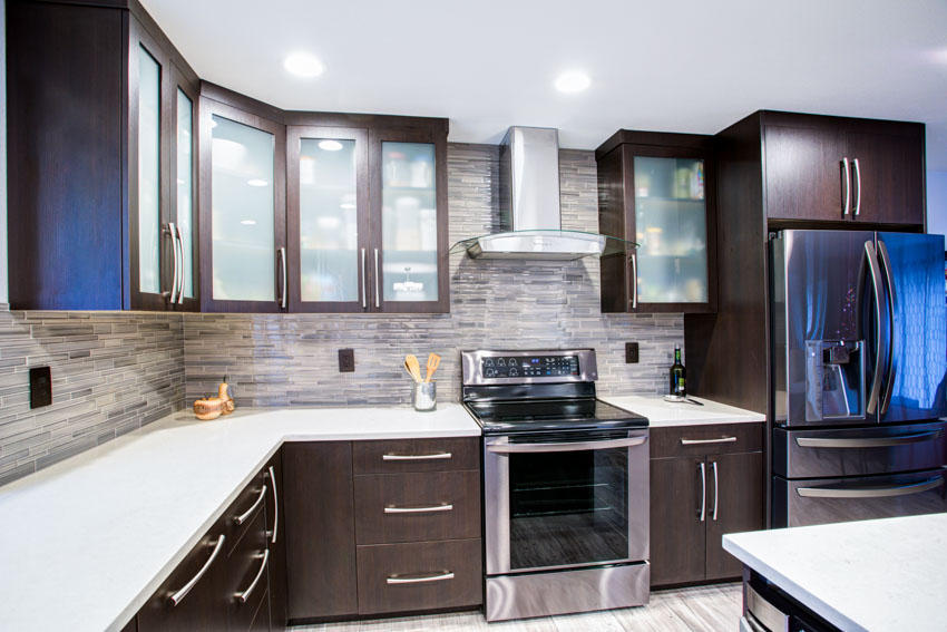 Kitchen with tile backsplash, range hood, frosted glass cabinets, oven, stove, countertop, and refrigerator