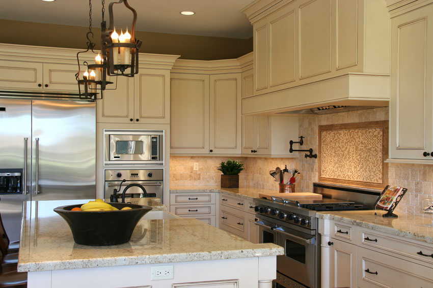 Kitchen with travertine backsplash, granite countertop, cabinets, pendant lights, stove, and refrigerator