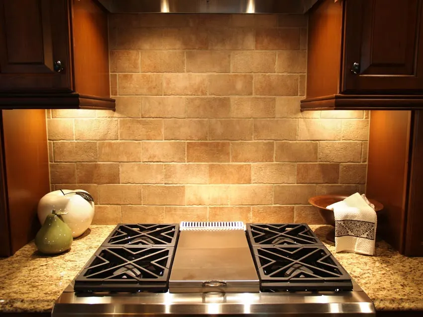 Kitchen with tumbled travertine backsplash, stove, cabinets, and countertop