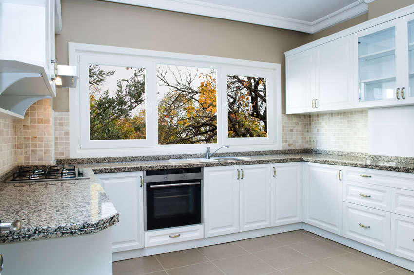 Kitchen with unglazed mosaic porcelain tile backsplash, tile floor, window, backsplash, cabinets, and oven