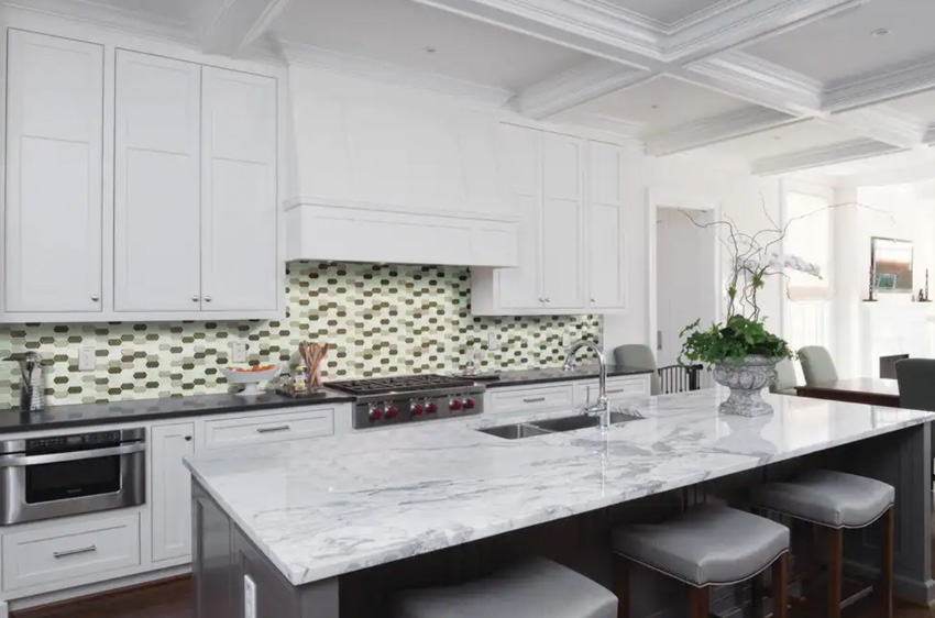 Kitchen with white cabinets, island, countertop, oven, stools, and picket tile backsplash